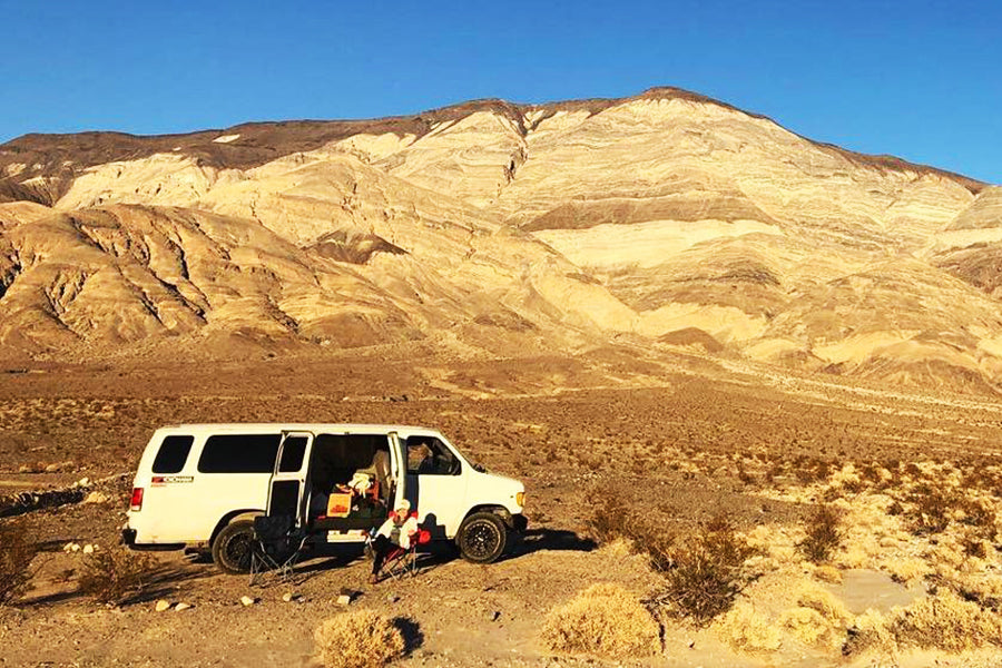 White RV rental in desert, huge mountains backdrop. Relaxing outside, perfect for your next adventure.
