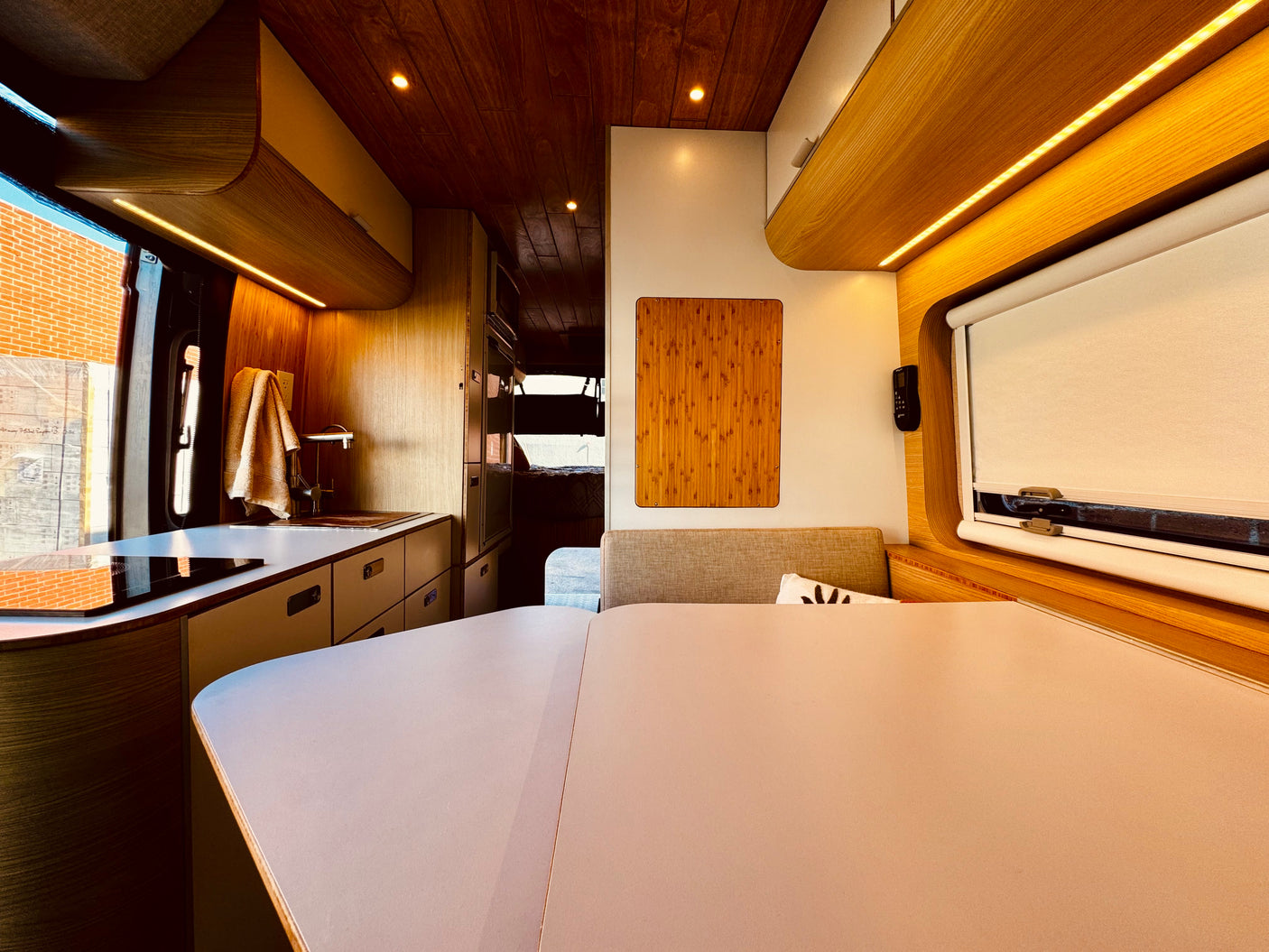 Modern RV rental interior: a sleek wood-paneled camper van featuring a kitchen, dining area, and ambient strip lighting.