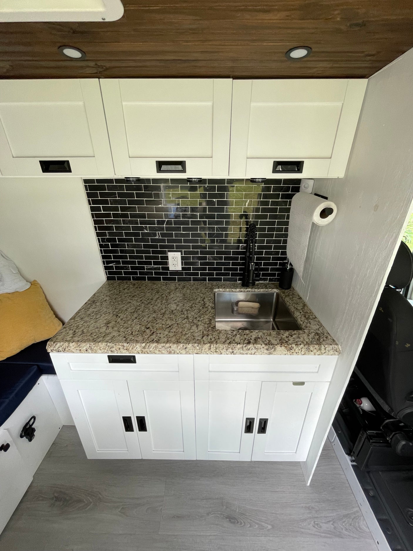 Modern RV rental kitchen: white cabinets, granite countertop, black subway tile backsplash, stainless sink, and wooden ceiling.