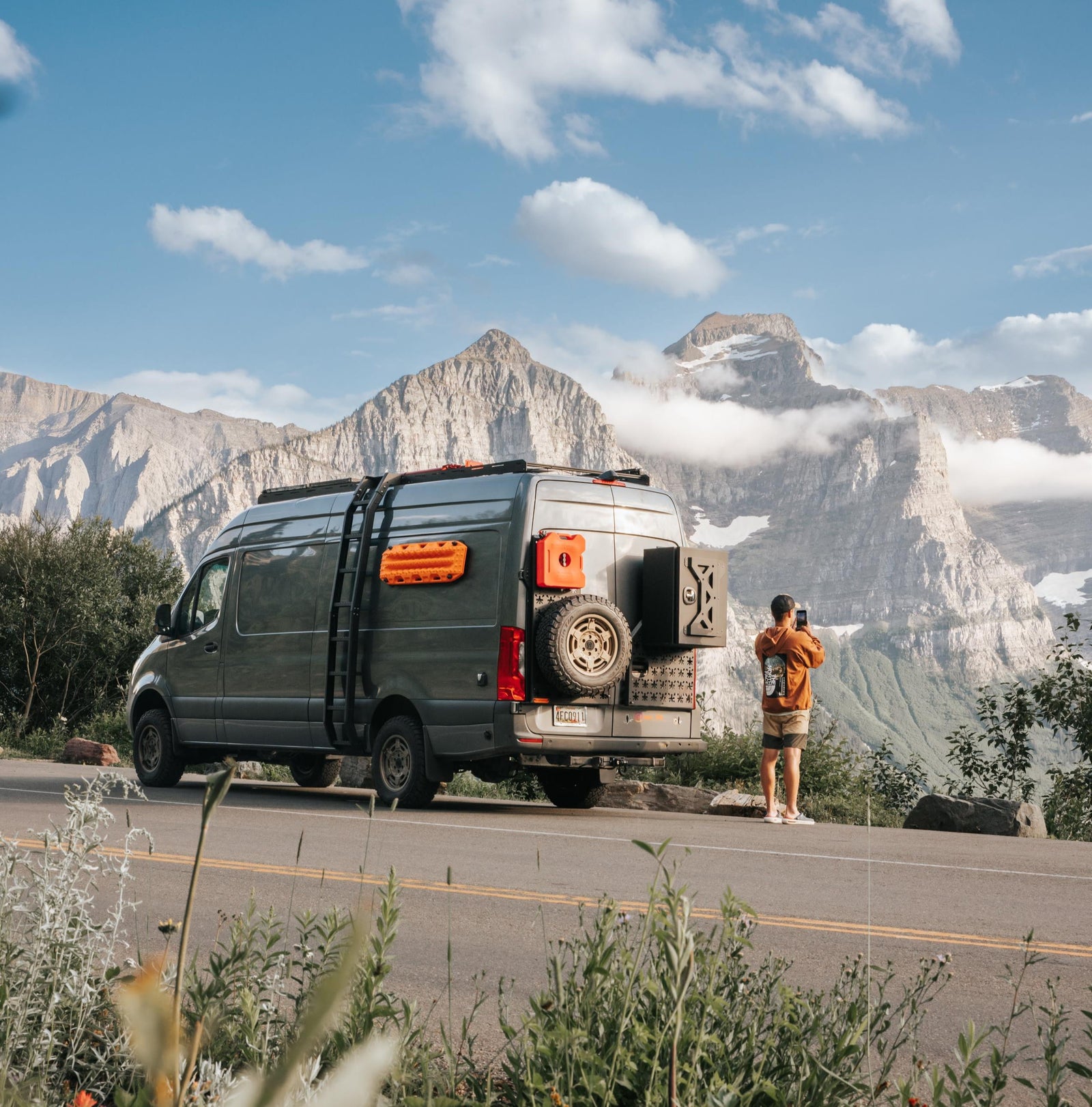 Custom rv rental van parked on mountain road as person photographs majestic