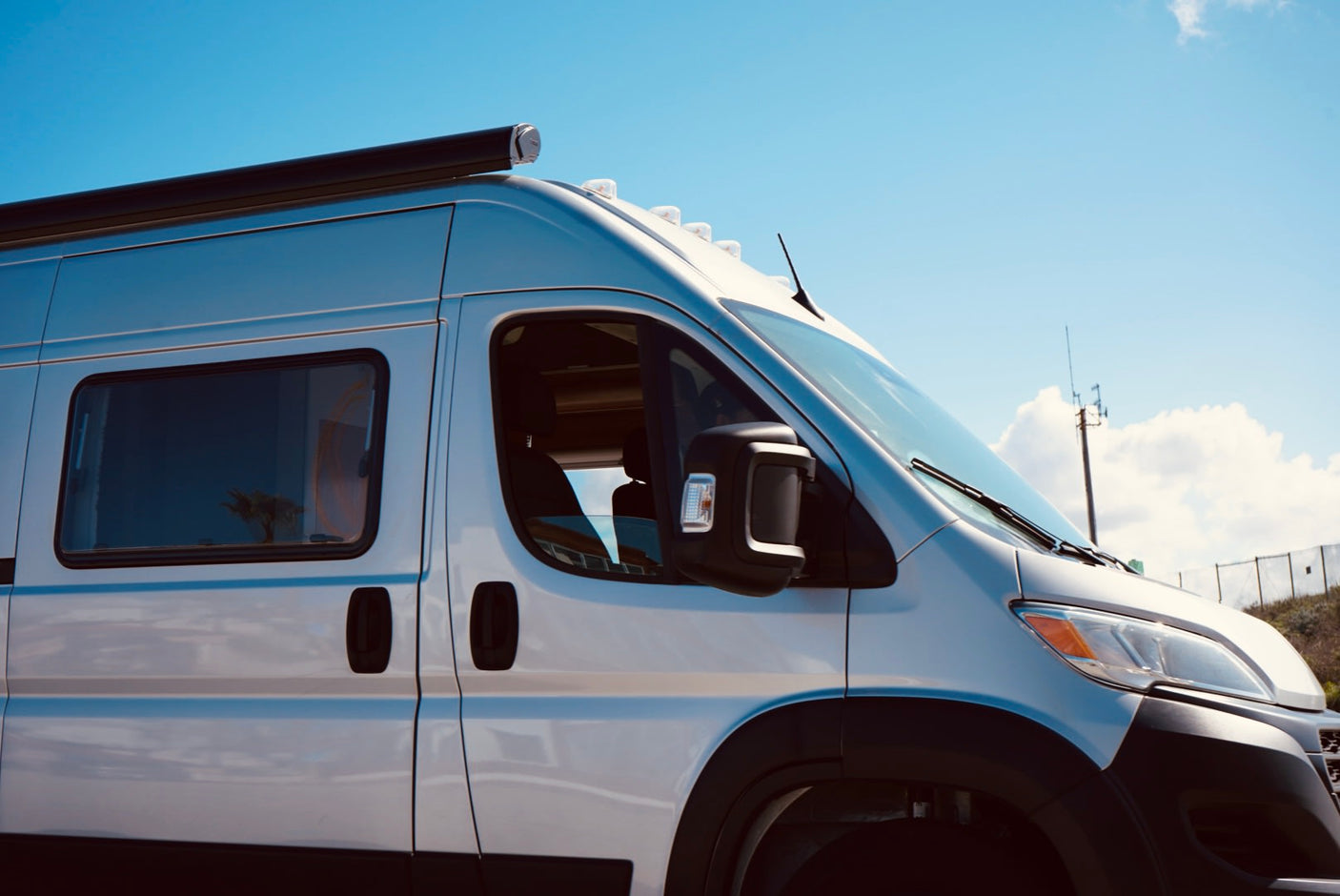 Modern white camper van, perfect for your next RV rental adventure. Equipped with an awning, under a clear blue sky.