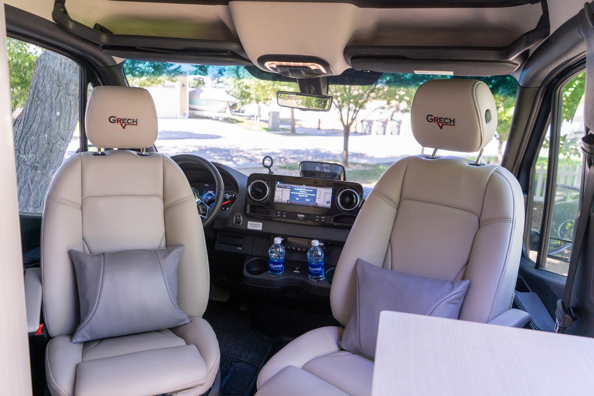 Inside this luxury RV rental: comfortable tan leather seats with grey pillows, a modern dashboard, and water bottles. — photo 12