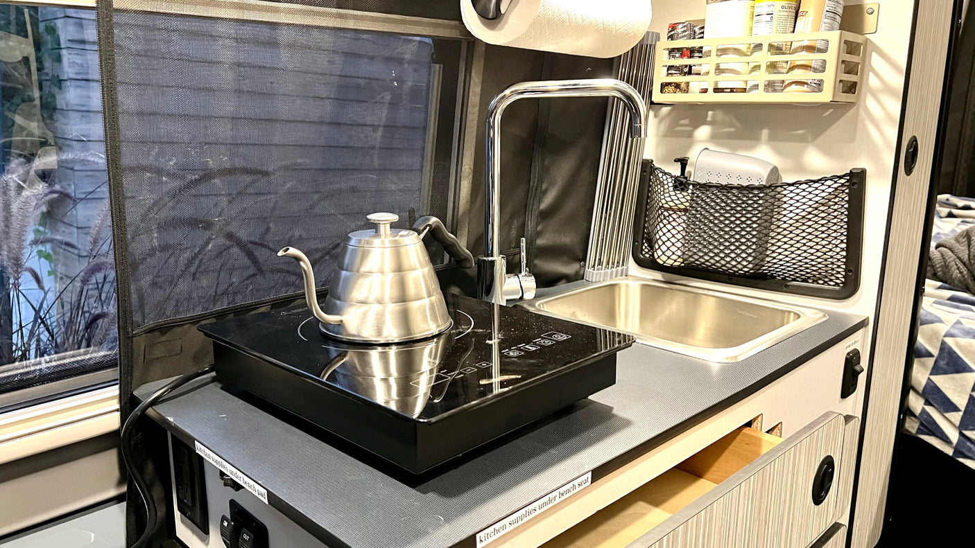 RV rental kitchen: induction cooktop with kettle, sink, and overhead storage. Ideal for compact travel cooking.