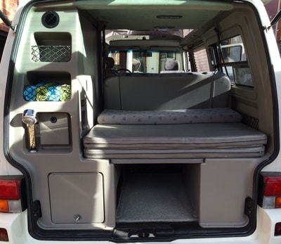 Compact rv rental camper van interior showing fold-down bed, built-in storage, and rear shower for easy travel.