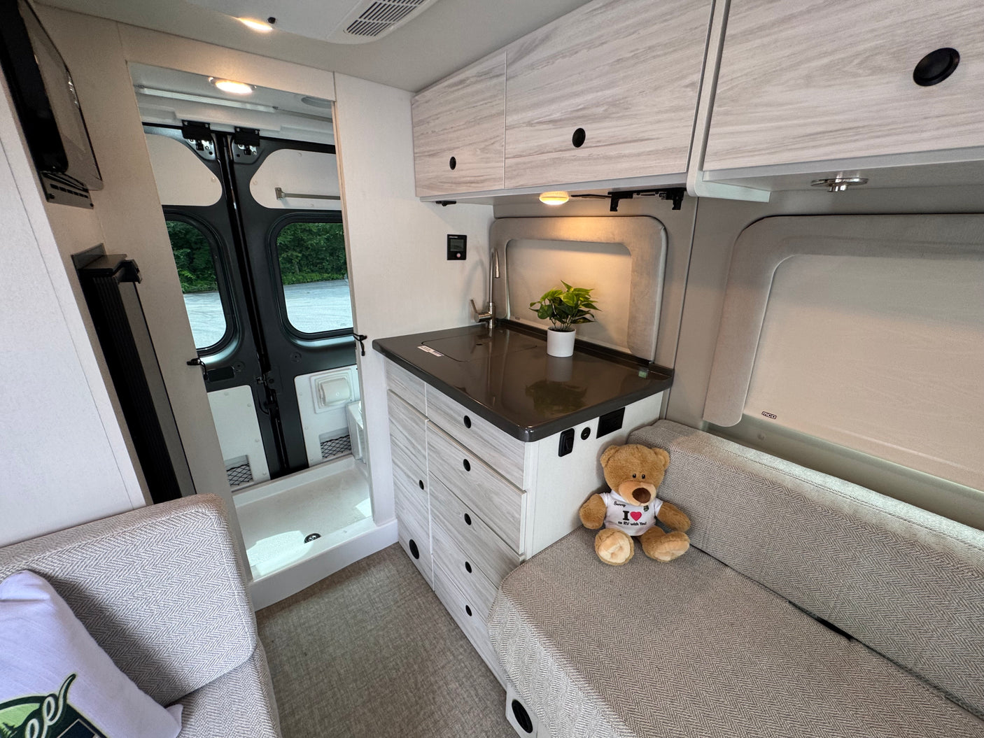 This modern RV rental interior features a functional compact kitchen, comfortable bench seating, and a built-in shower.