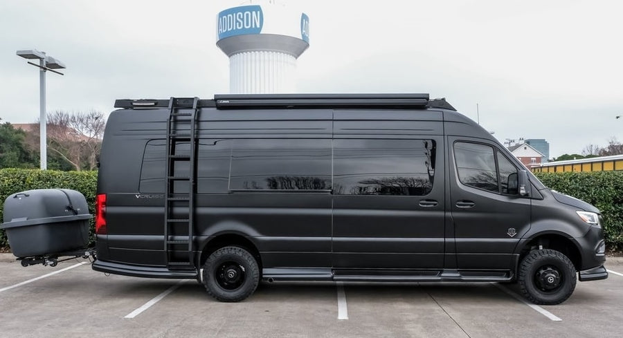 This matte black adventure RV rental, a custom Sprinter van with off-road tires and a rear cargo trailer, awaits you.