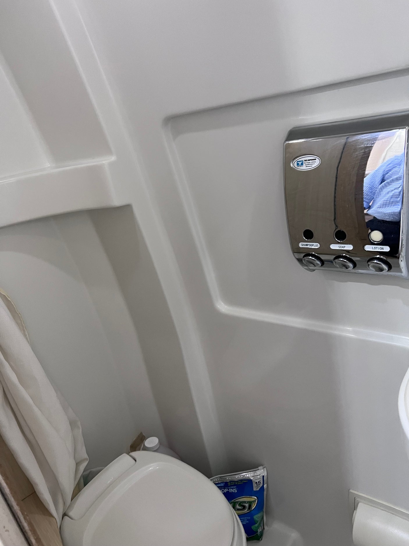 View of a space-saving RV rental bathroom with a toilet, shower area, and chrome soap dispenser.