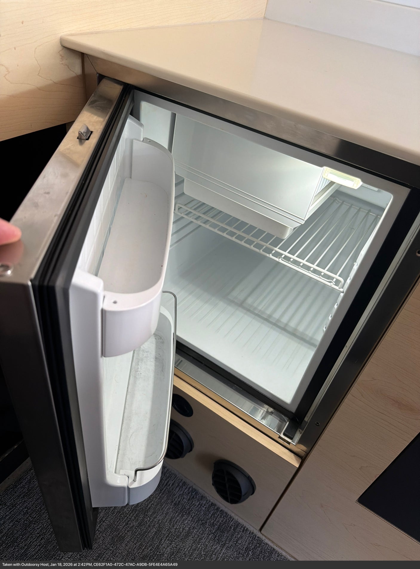 This RV rental features a clean, empty mini-fridge with wire shelves and door storage, illuminated and ready for use.
