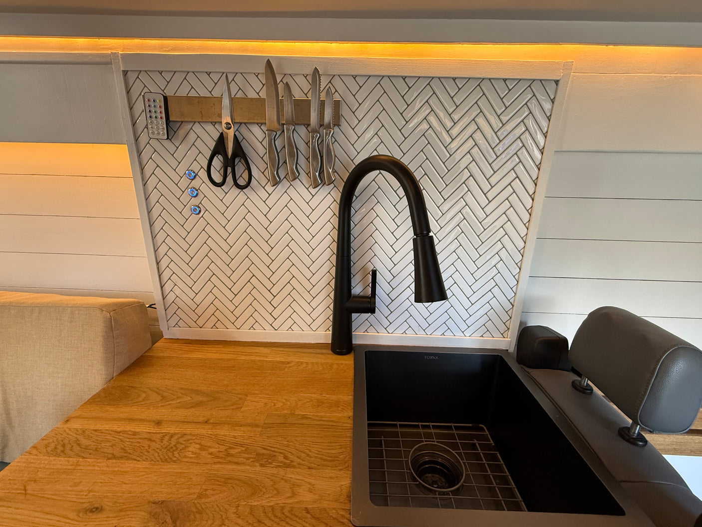 Compact rv rental kitchen: sleek black faucet, sink, wood countertop, and smart magnetic knife storage on a herringbone backsplash.