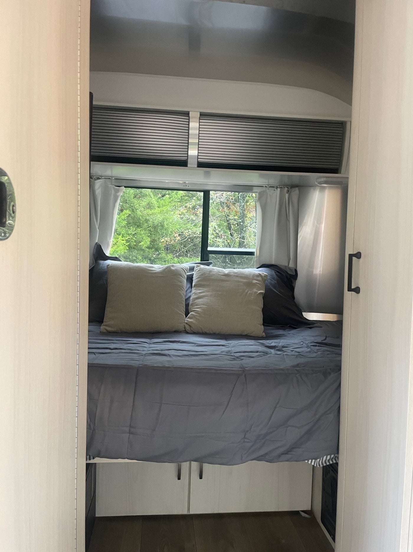 Relaxing rv rental bedroom interior, featuring a comfy bed with grey bedding, pillows, and a window view of lush trees. — photo 7