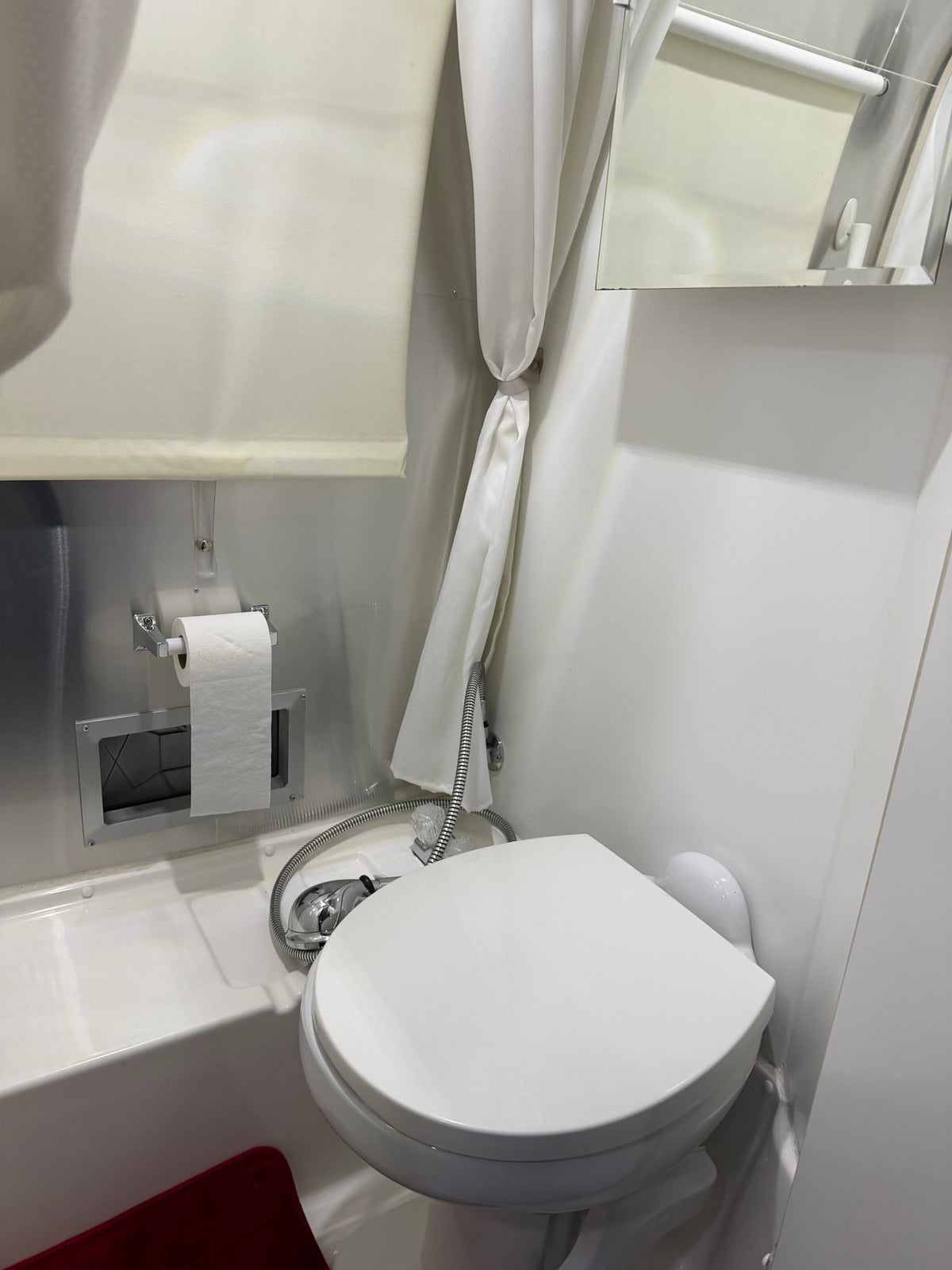 Compact RV rental bathroom: toilet, shower, and toilet paper dispenser over tub, with a tied-back shower curtain. — photo 6