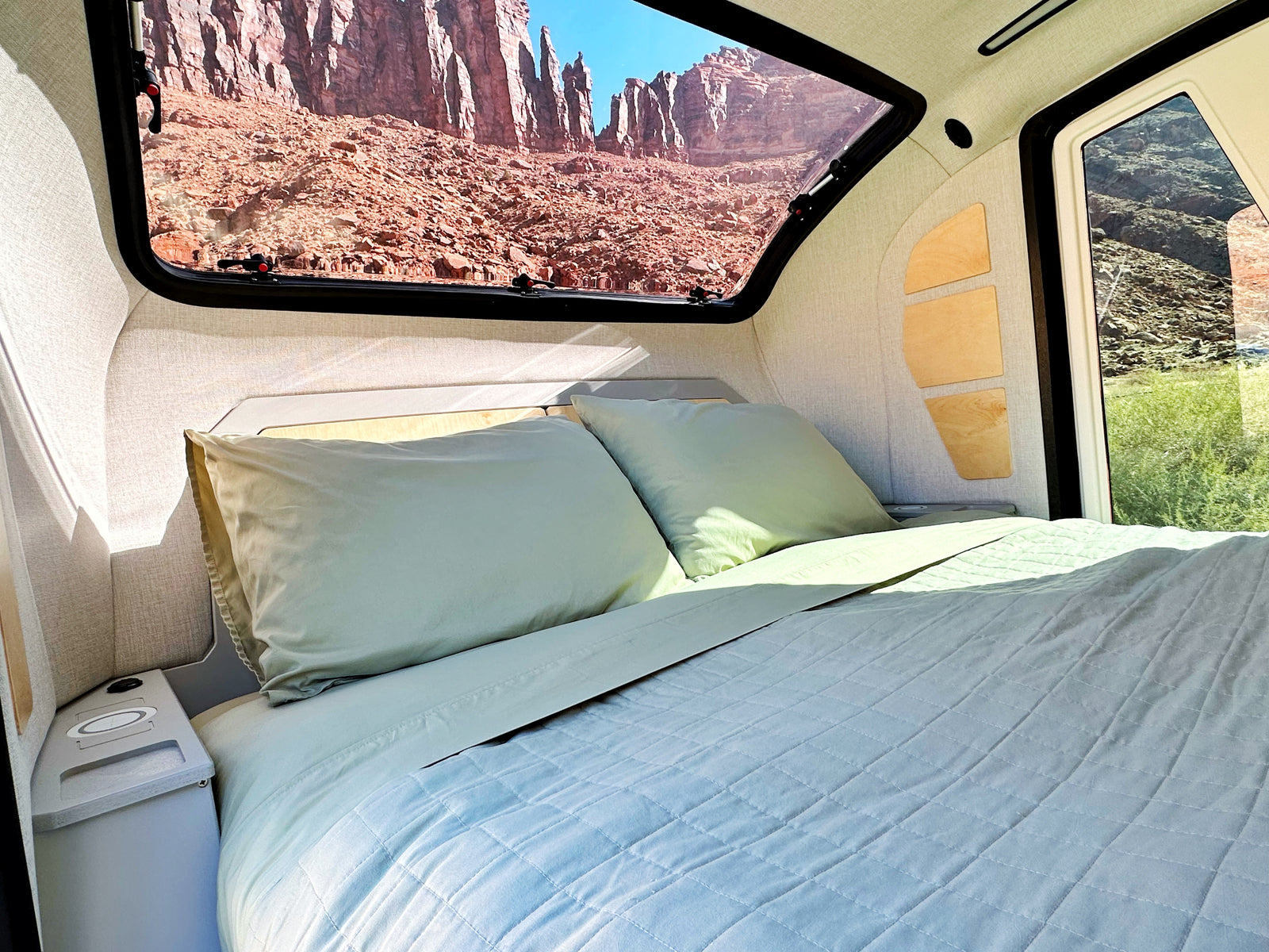 RV rental: Inside a modern camper with a comfy bed & scenic window view of red rocks.