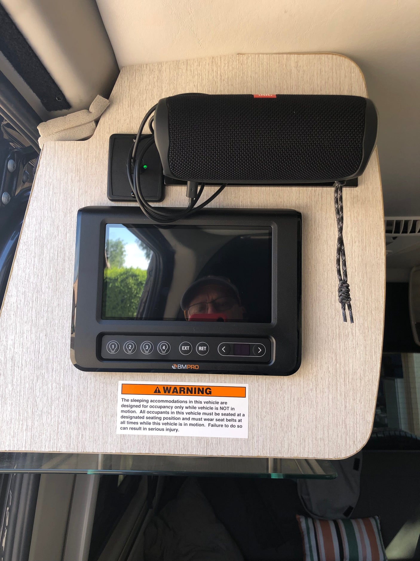 RV rental interior: BMPro control panel & JBL speaker. Safety warning. Screen reflects user & outdoors.