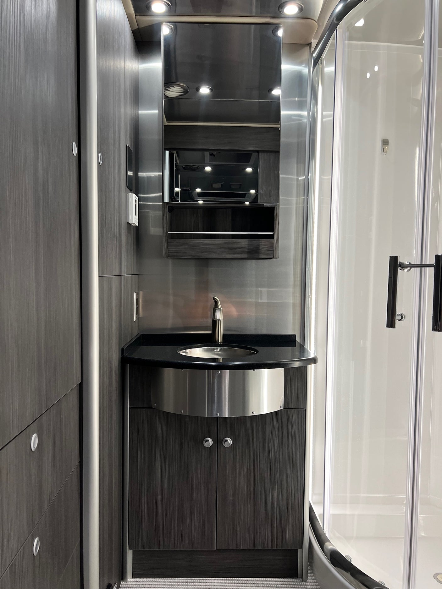 Modern RV rental bathroom: sleek vanity with sink, mirror, and curved shower enclosure.