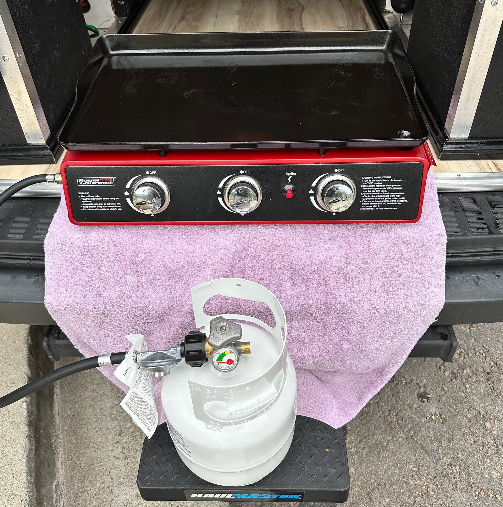 RV rental outdoor cooking setup: Red gas griddle & white propane tank on step, ready for camping meals.