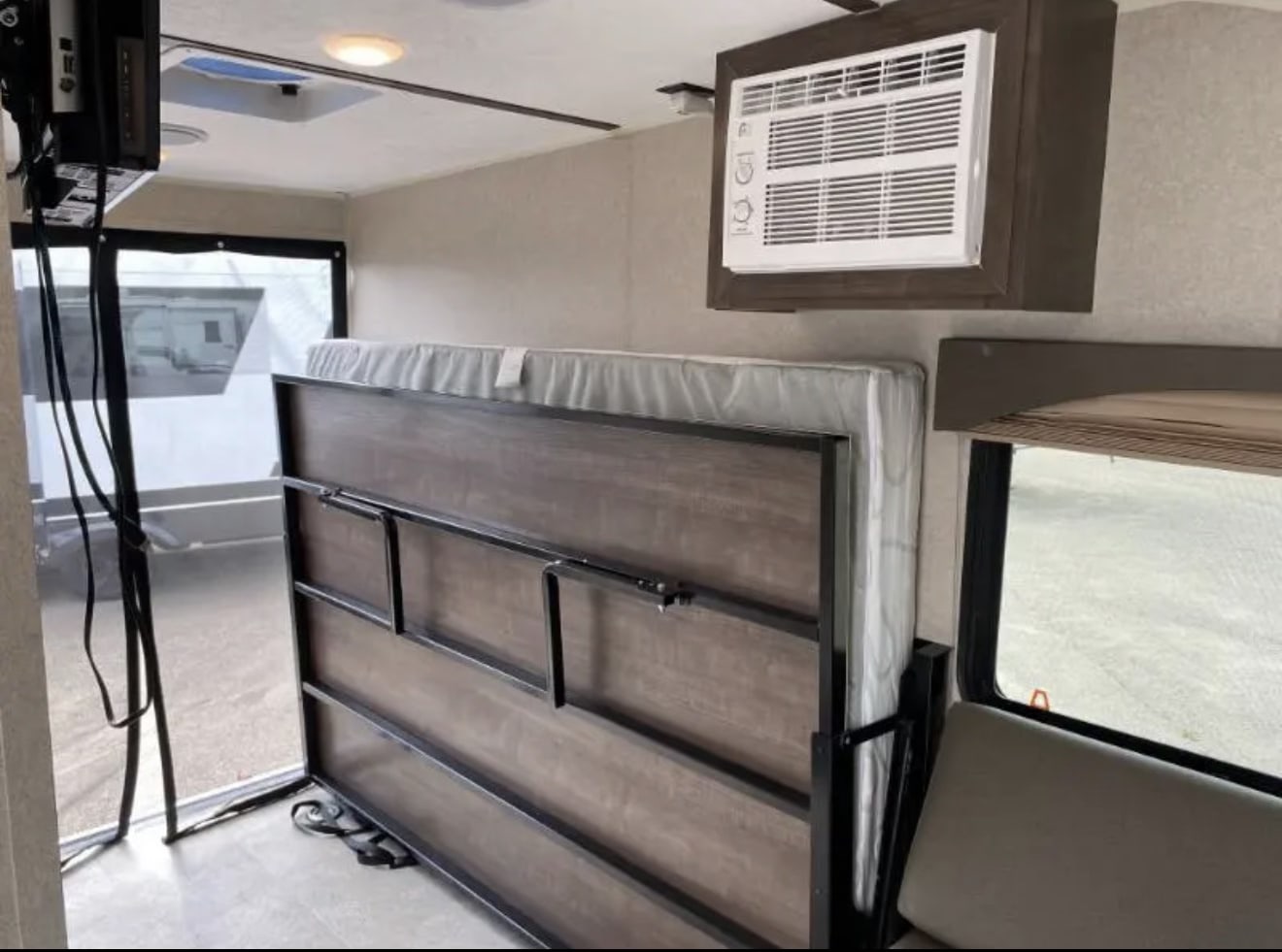 and cabinets.|Compact RV rental bedroom with a comfy white patterned mattress. Window view shows another RV outside