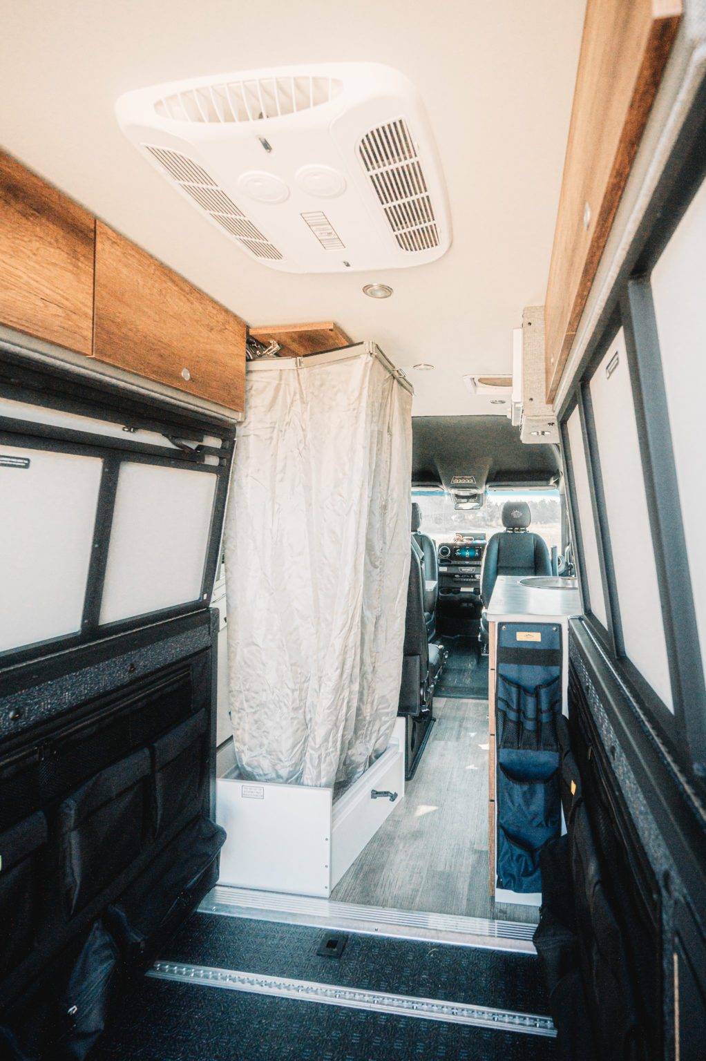 RV rental interior of a camper van, featuring an AC unit, wooden cabinets, and a pull-out shower, offering comfortable living.