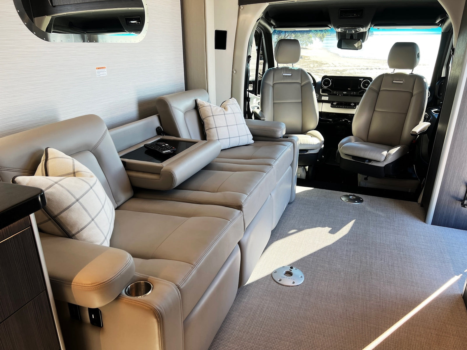 Inside this RV rental, a comfy light leather sofa and convertible seating fill the cabin, facing the cockpit and road view.