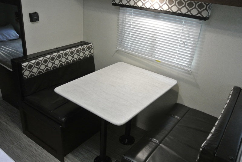 **RV rental**'s compact dinette area, featuring a white table, patterned bench seating, and window blinds.