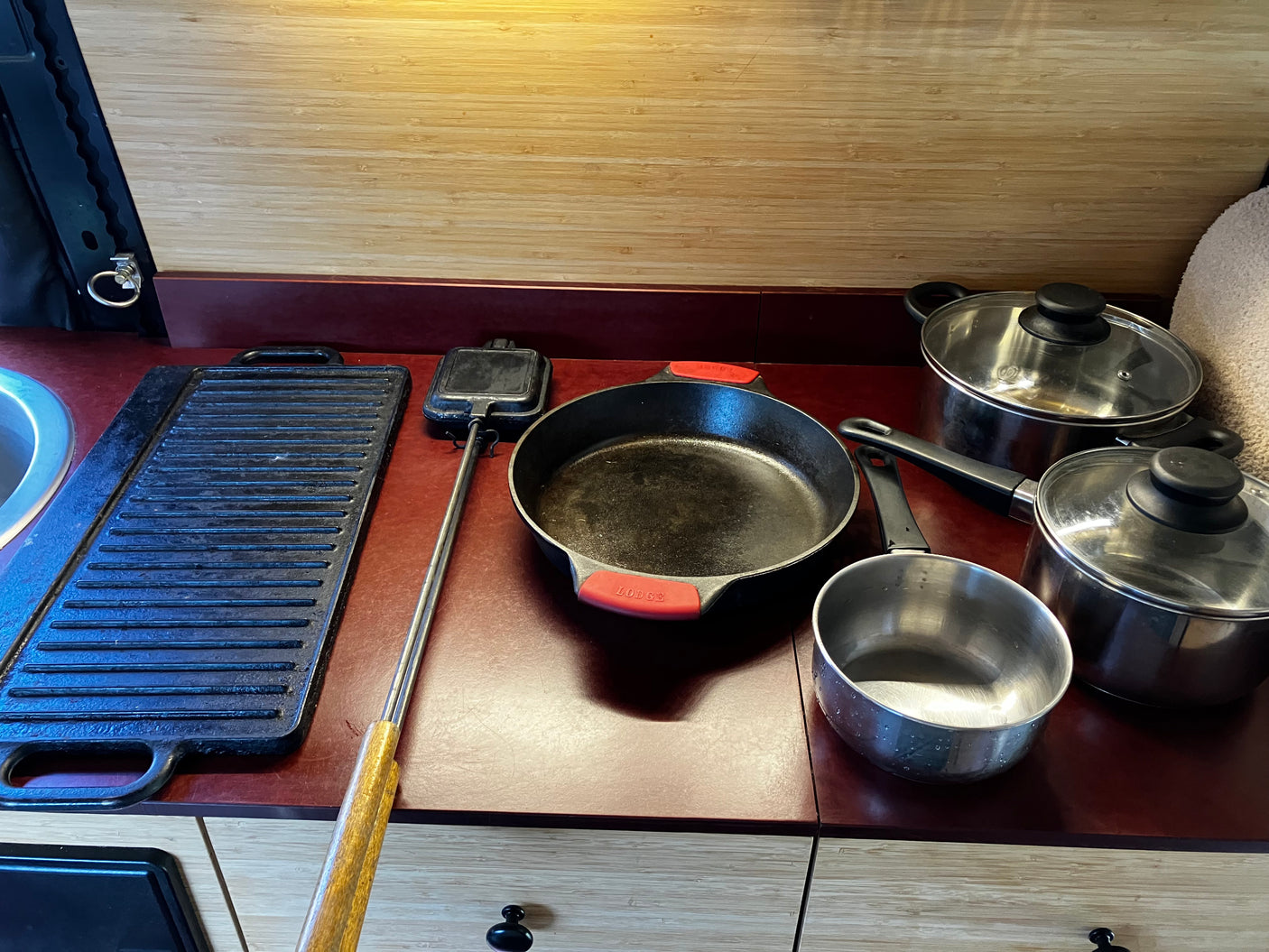RV rental kitchen: counter with cast iron skillet, griddle, pie iron, and stainless steel pots & pans ready for cooking.