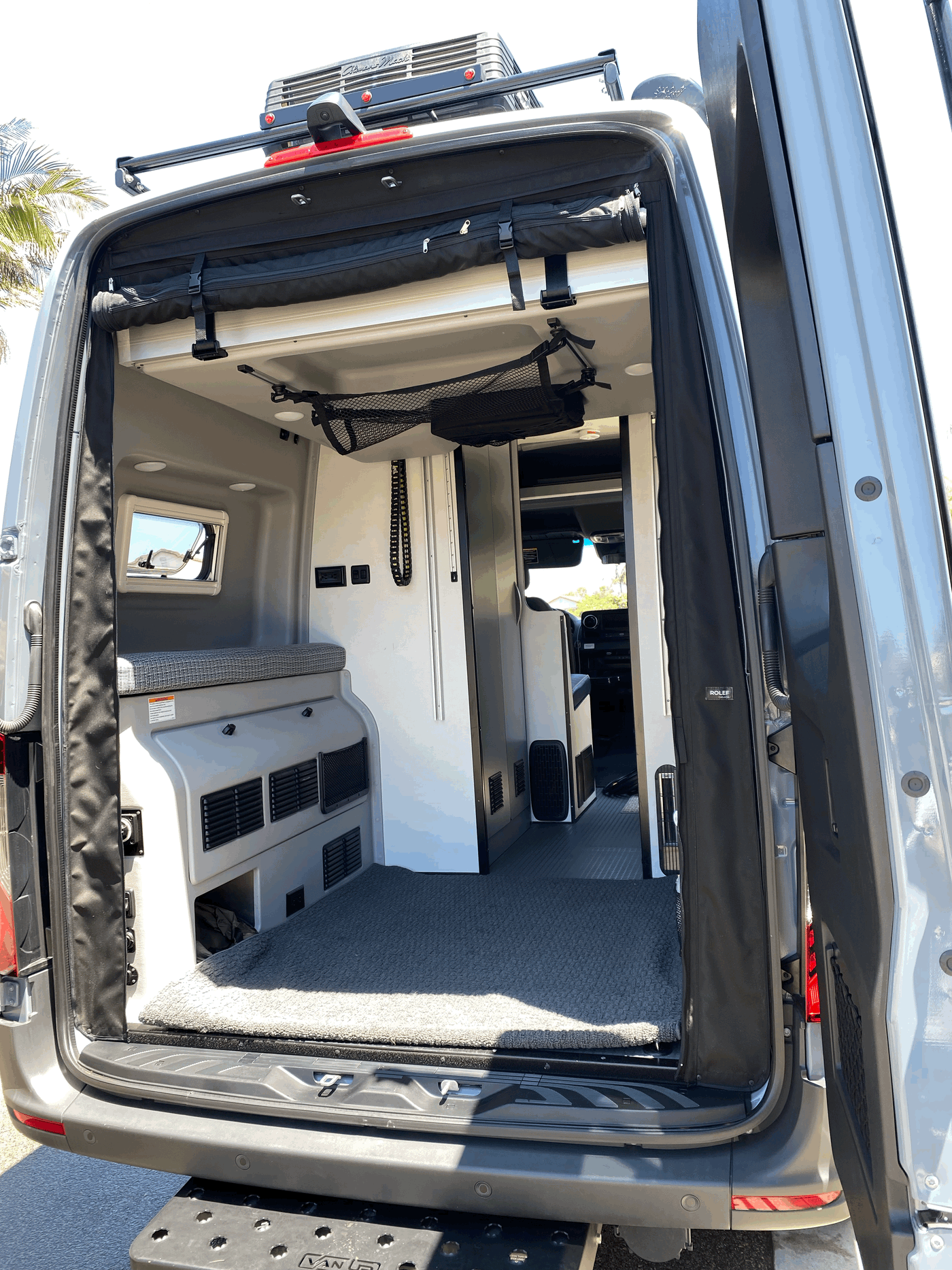 RV rental camper van interior from back: features elevated bed with cushion, built-in storage, and overhead mesh netting. — photo 7