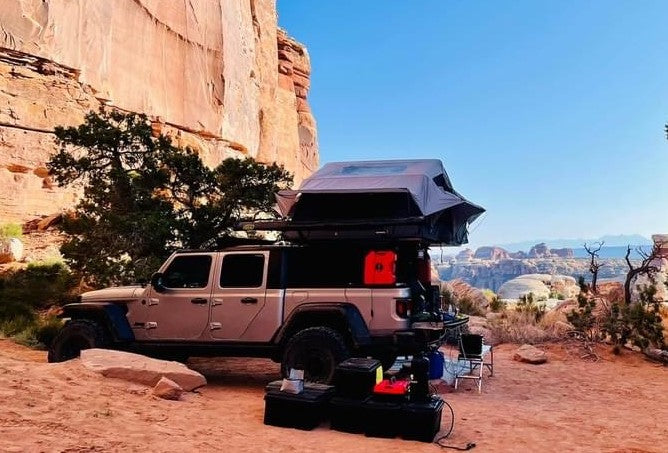 Jeep Gladiator with rooftop tent deployed, a unique RV rental for overlanding. Camping in a vast red rock canyon.