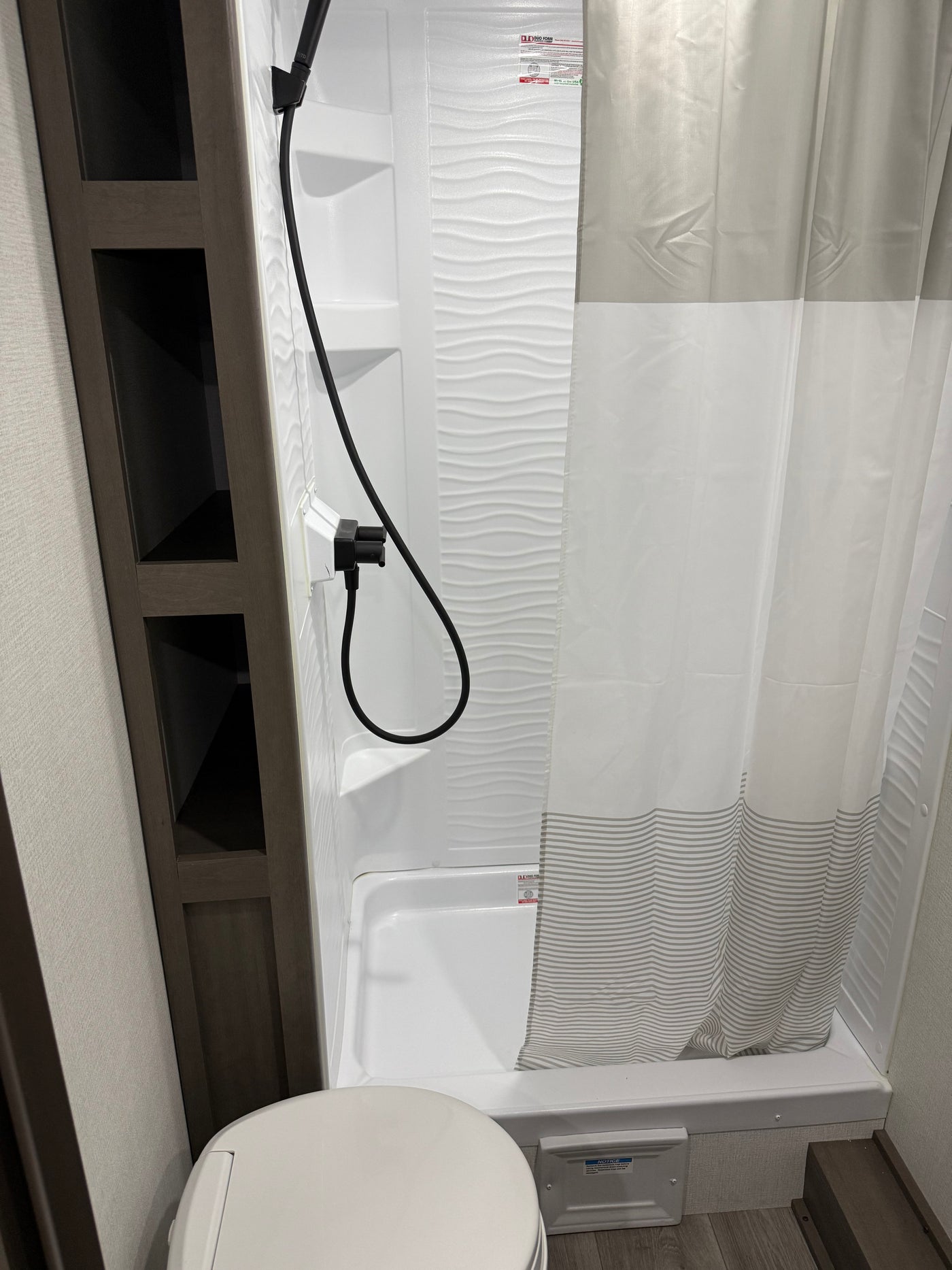 Experience this clean RV rental bathroom with a shower, wavy-textured wall, striped curtain, toilet, and convenient shelving. — photo 4