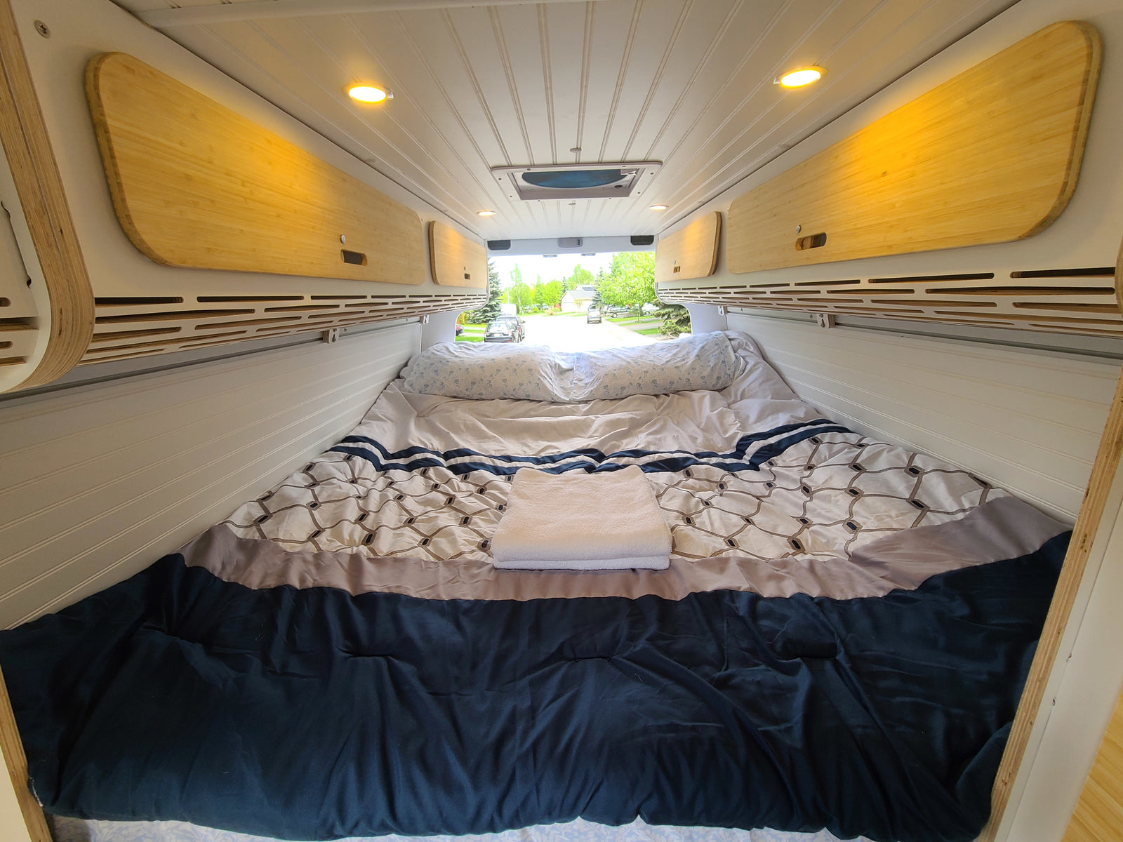 RV rental bedroom: cozy bed, warm bamboo overhead storage, and bright ceiling lights for comfort.