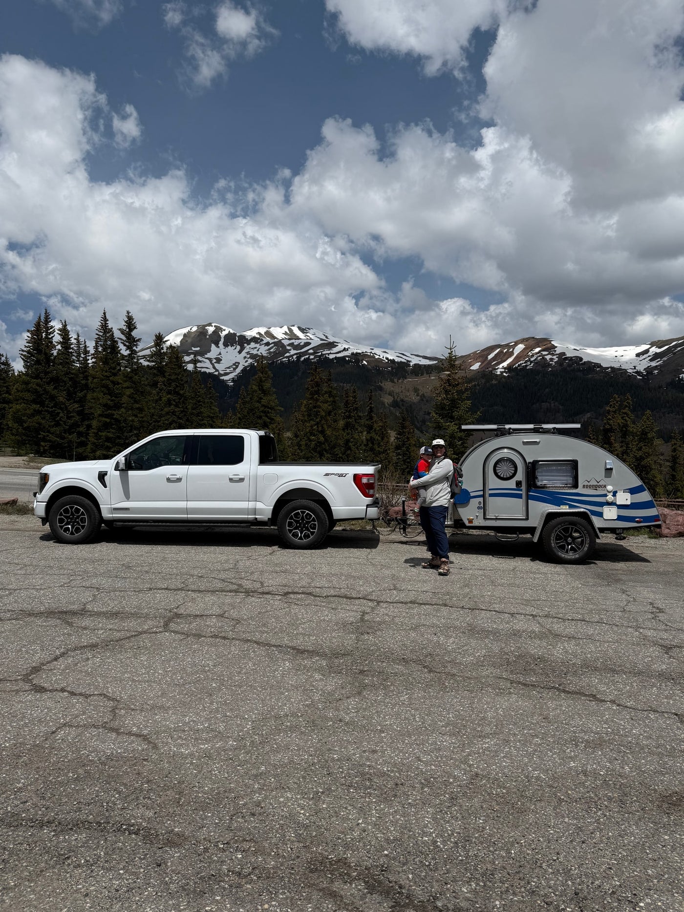 Mountain rv rental trip: White truck, teardrop camper, adult holding child, against snowy peaks & cloudy sky. — photo 6