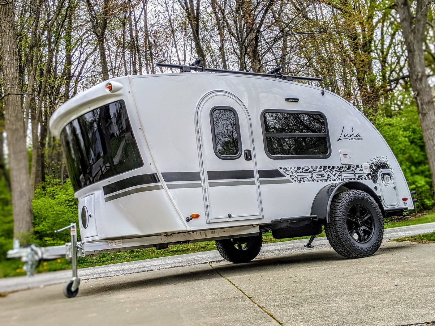 Sleek white Luna Rover teardrop travel trailer with a roof rack & rugged tires, ready for your next rv rental adventure.
