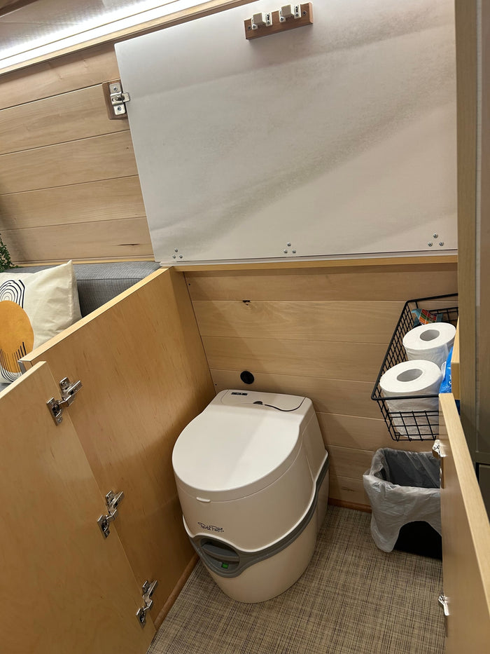 RV rental: A compact, clean Thetford portable toilet is integrated into a wooden enclosure with storage for toilet paper.