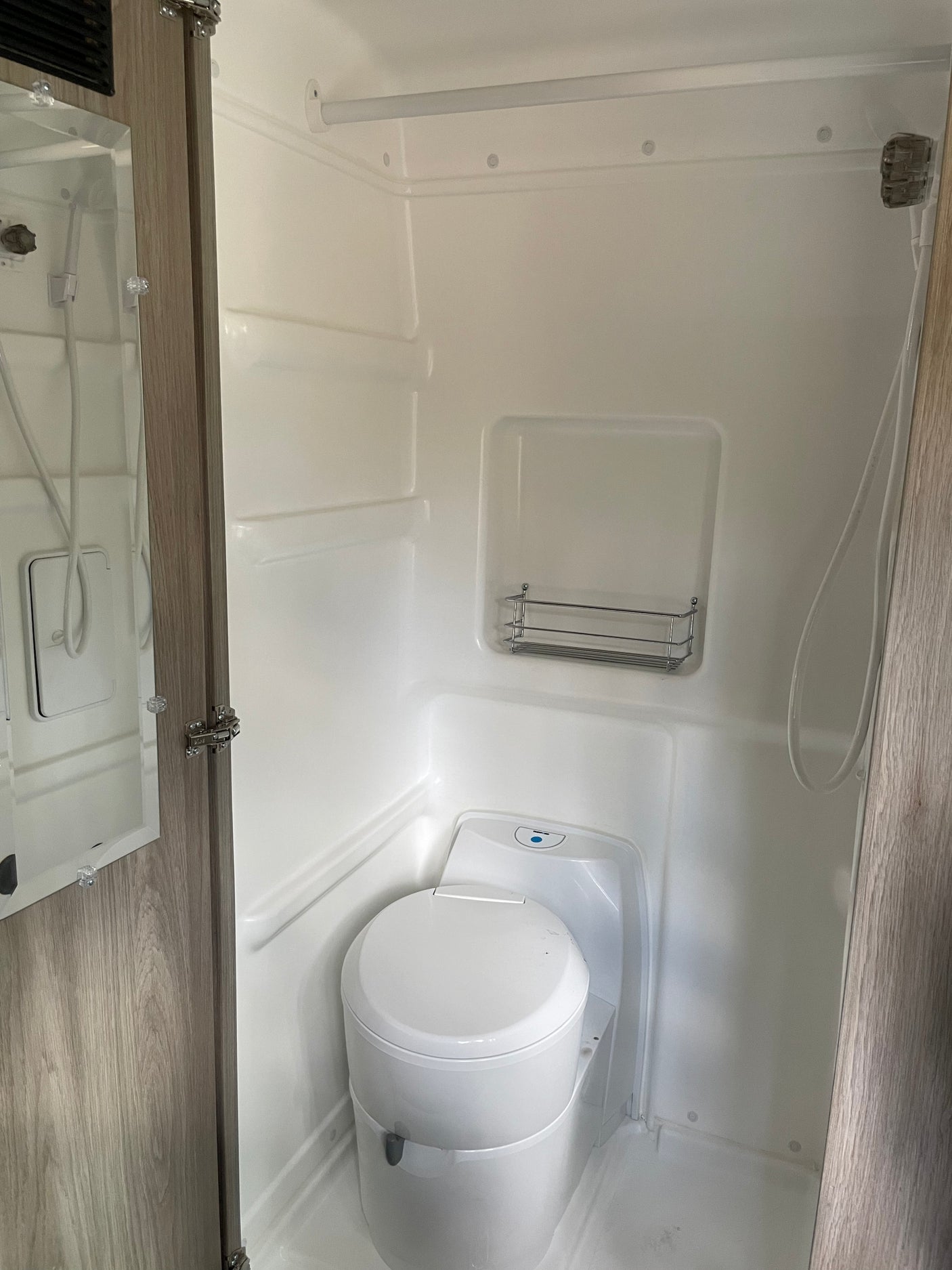 This RV rental's compact bathroom includes an integrated white shower, a modern cassette toilet, and a mirrored cabinet.