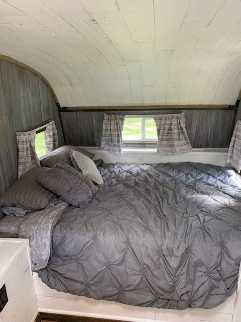 Cozy RV rental bedroom: gray bed, white shiplap, and rustic wood-paneled accent wall with a window.