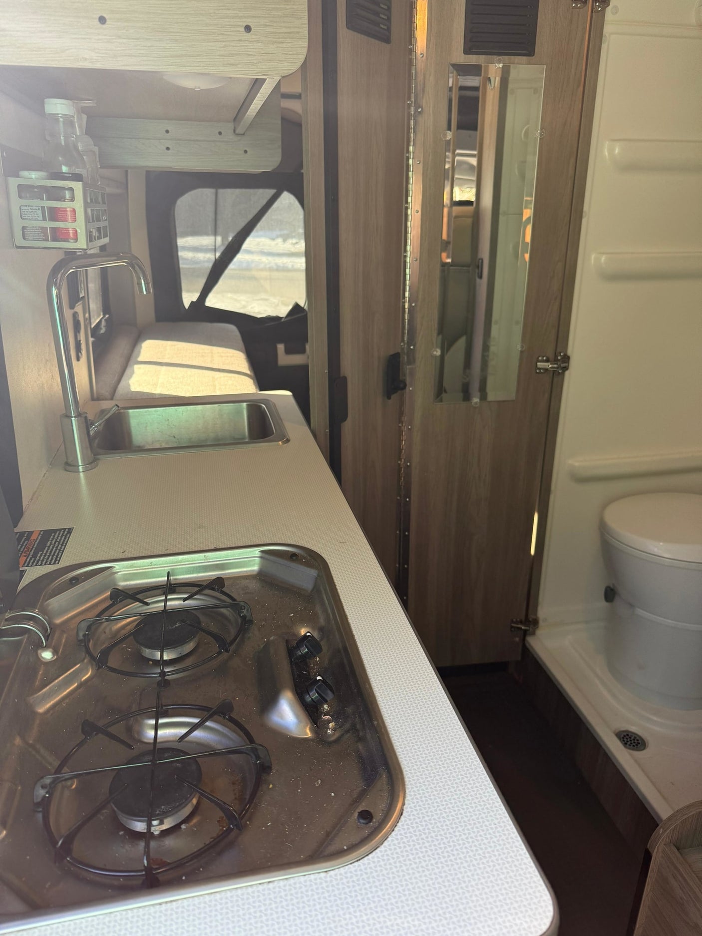 Functional RV rental interior: kitchen with sink and two-burner stove, next to a compact bathroom with toilet and shower.