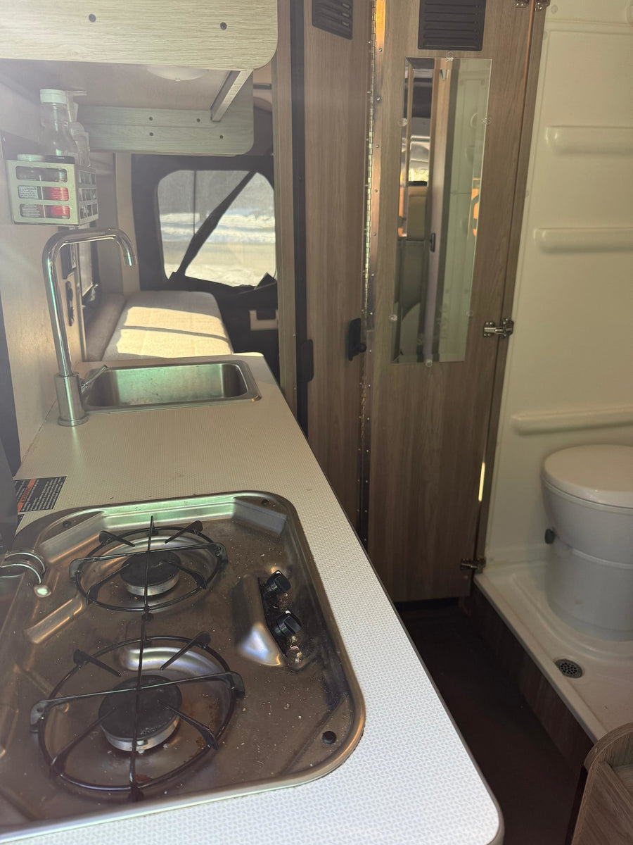 Functional RV rental interior: kitchen with sink and two-burner stove, next to a compact bathroom with toilet and shower.