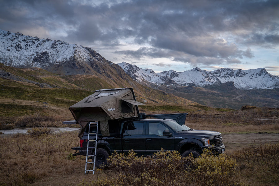 Adventure awaits! Black F-150 with a rooftop tent, a rugged RV rental option, parked in snowy mountains.