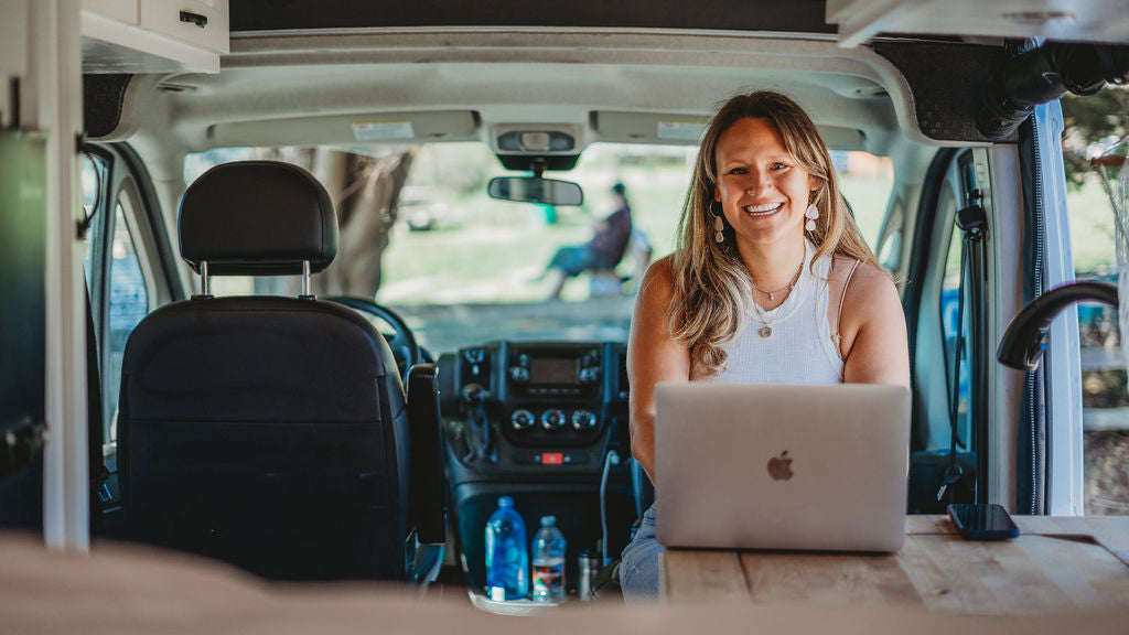 Smiling woman on laptop in RV rental. This mobile office highlights van life and remote work flexibility for travel.