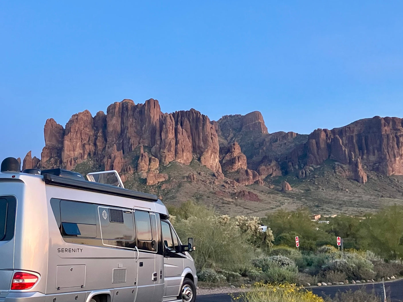 Silver 'Serenity' RV rental camper van parked by desert plants, facing majestic, rugged mountains under a clear sky.