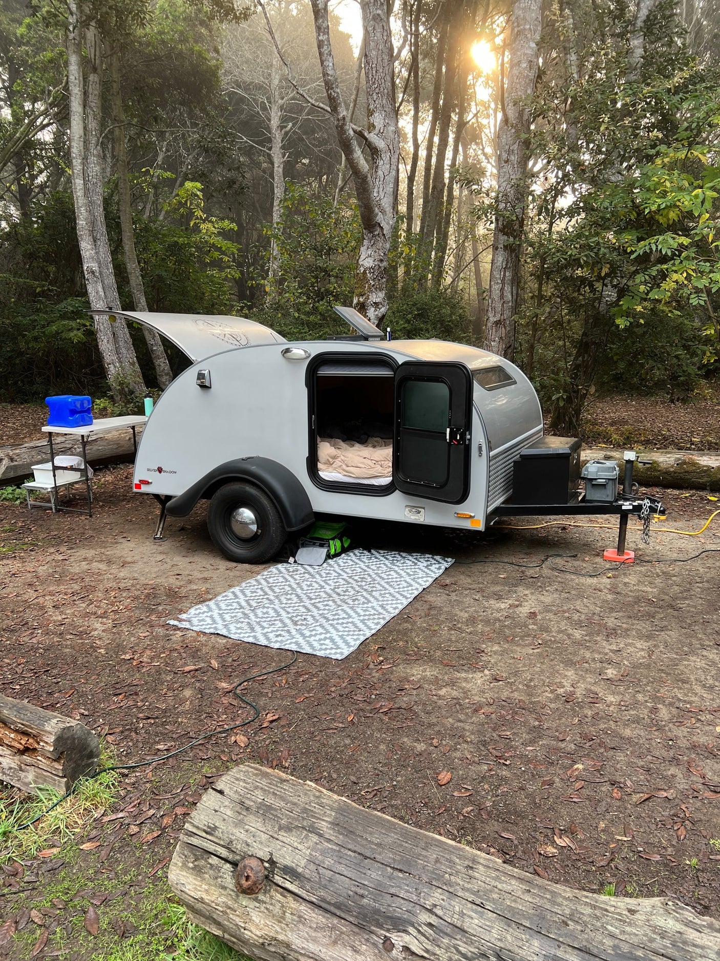 with a cozy bed visible inside.|Scenic RV rental trip! A teardrop camper by a golden autumn vineyard