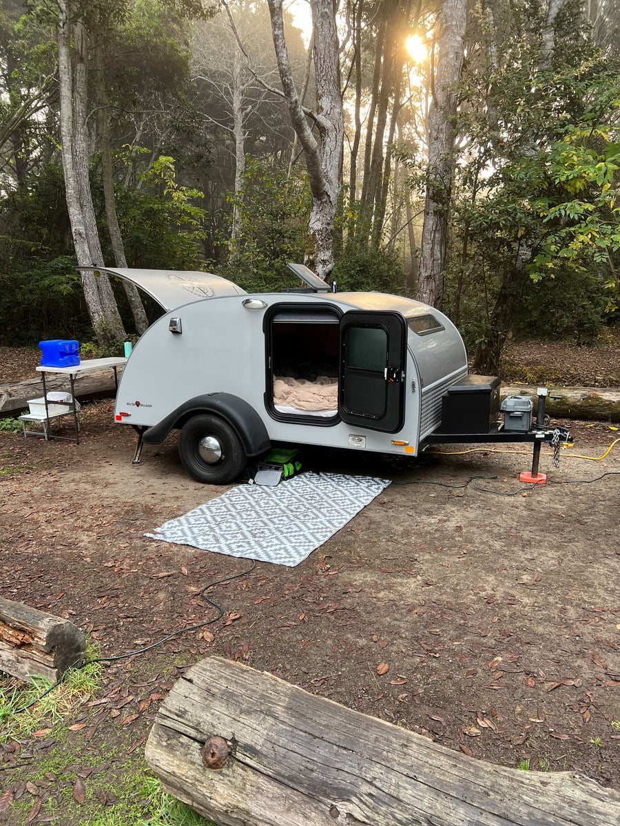 with a cozy bed visible inside.|Scenic RV rental trip! A teardrop camper by a golden autumn vineyard