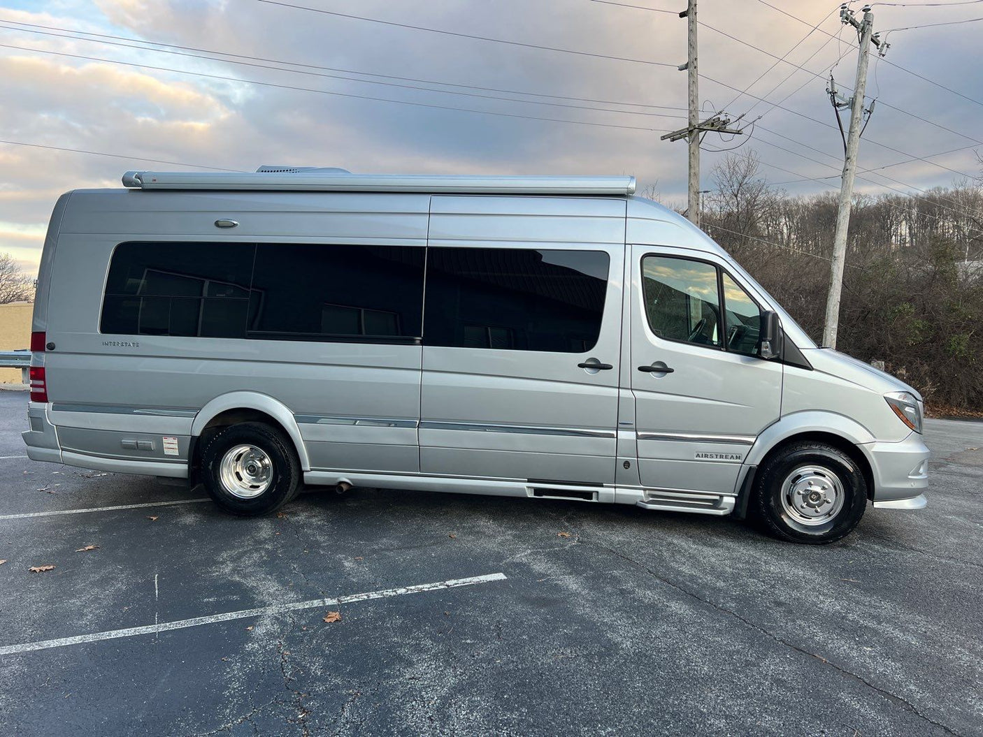 Side view of a sleek silver Airstream Interstate RV rental van under a cloudy sky. Ideal for comfortable travel.