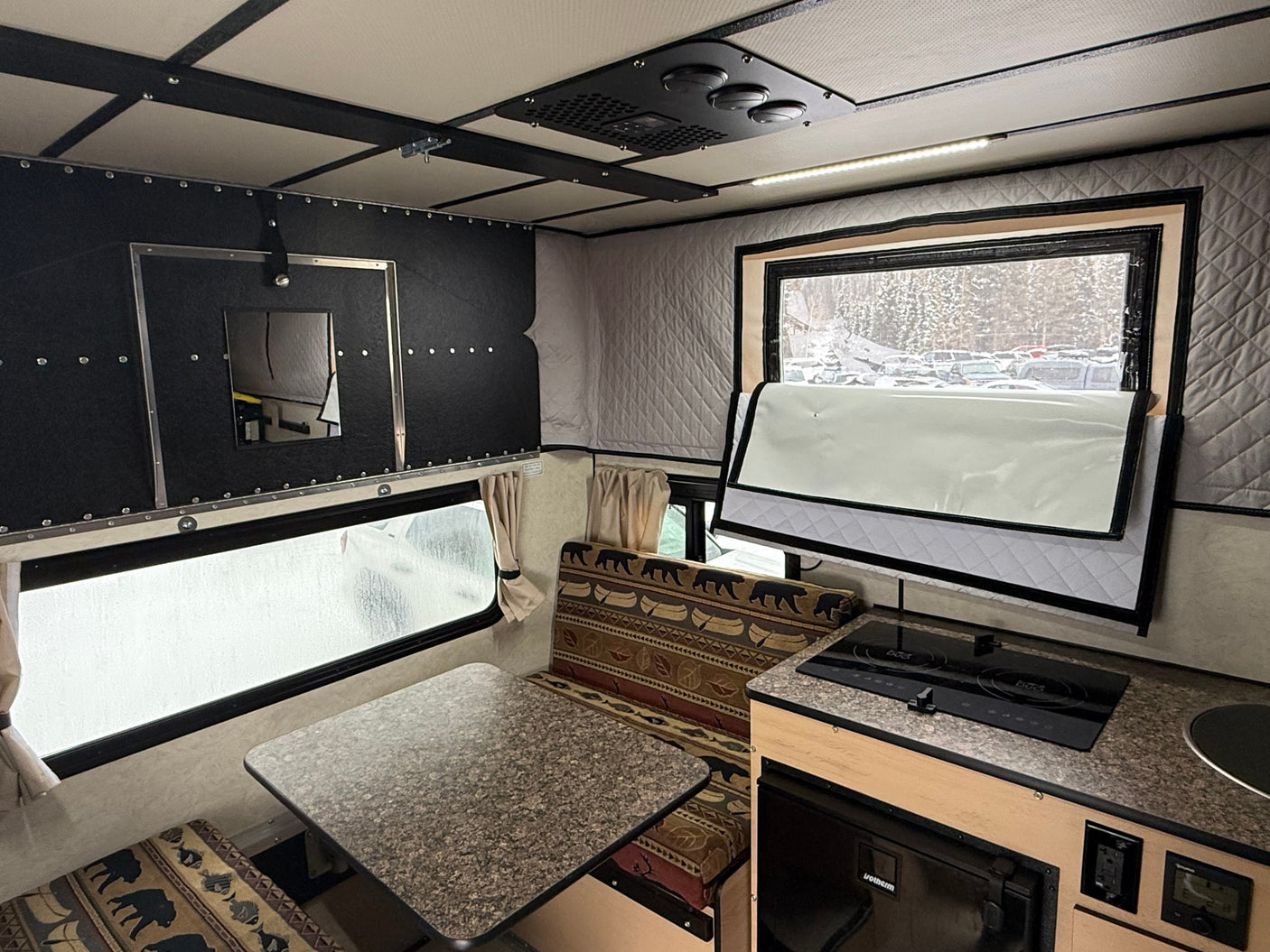 Experience this RV rental's cozy interior with a kitchenette, dining area, and insulated windows offering a snowy outdoor view.