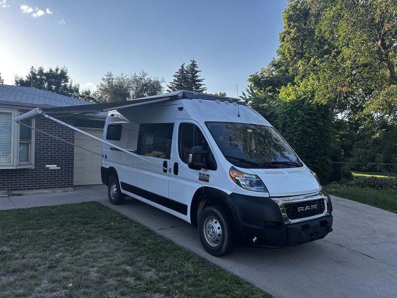White Ram ProMaster camper van with extended awning parked on a driveway. Ideal for your next rv rental adventure.