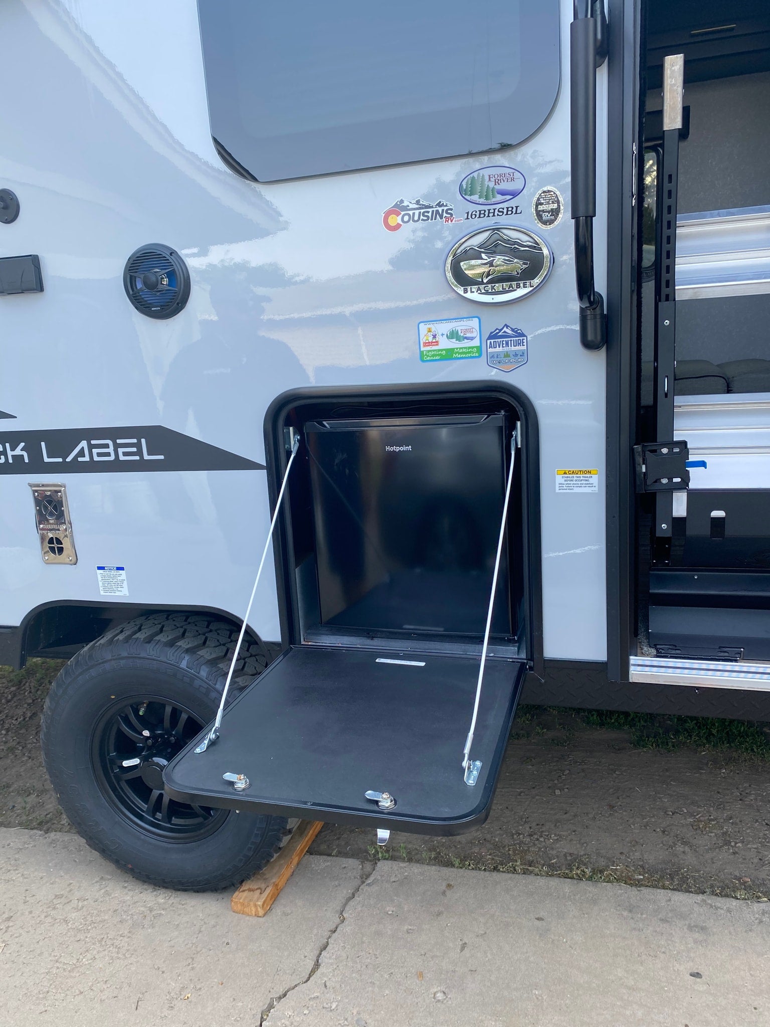 This rv rental offers outdoor convenience with an open exterior hatch revealing a Hotpoint mini-fridge and a pull-down table.