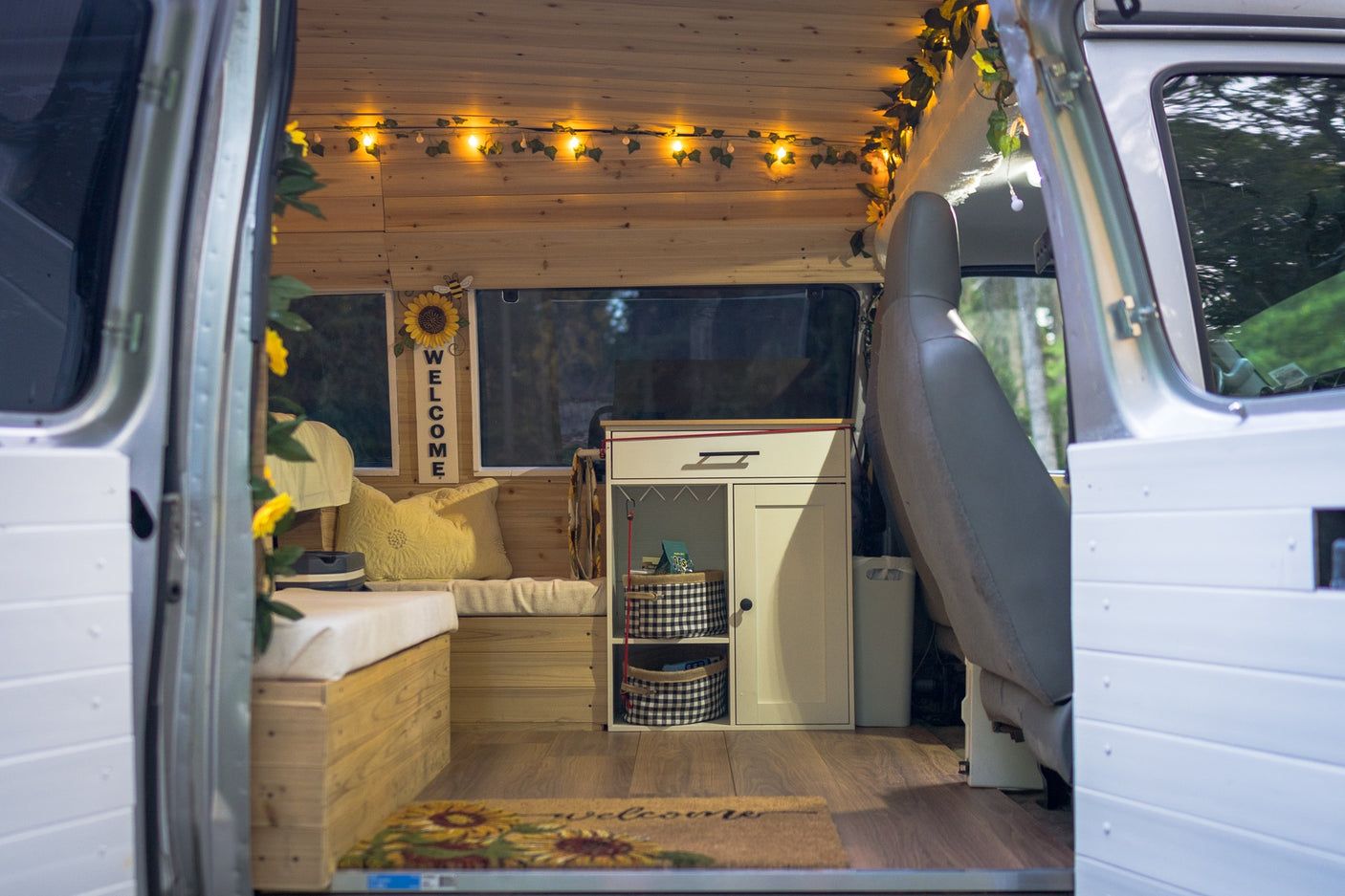 Cozy RV rental interior: wood paneling, string lights, "Welcome" sign, and organized storage for comfortable travel.