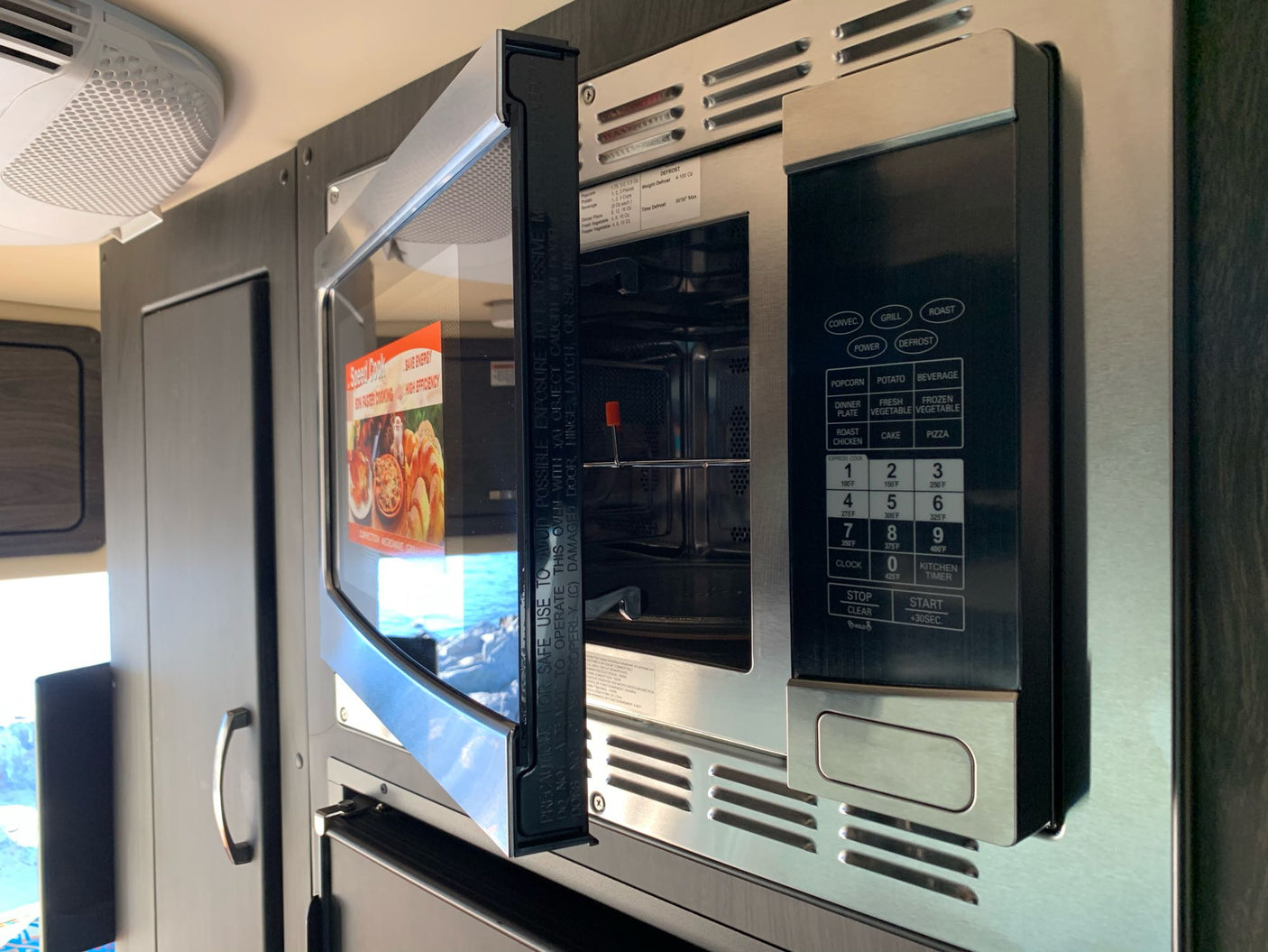 RV rental kitchen features a stainless steel convection microwave oven, door open, for easy cooking and defrosting.