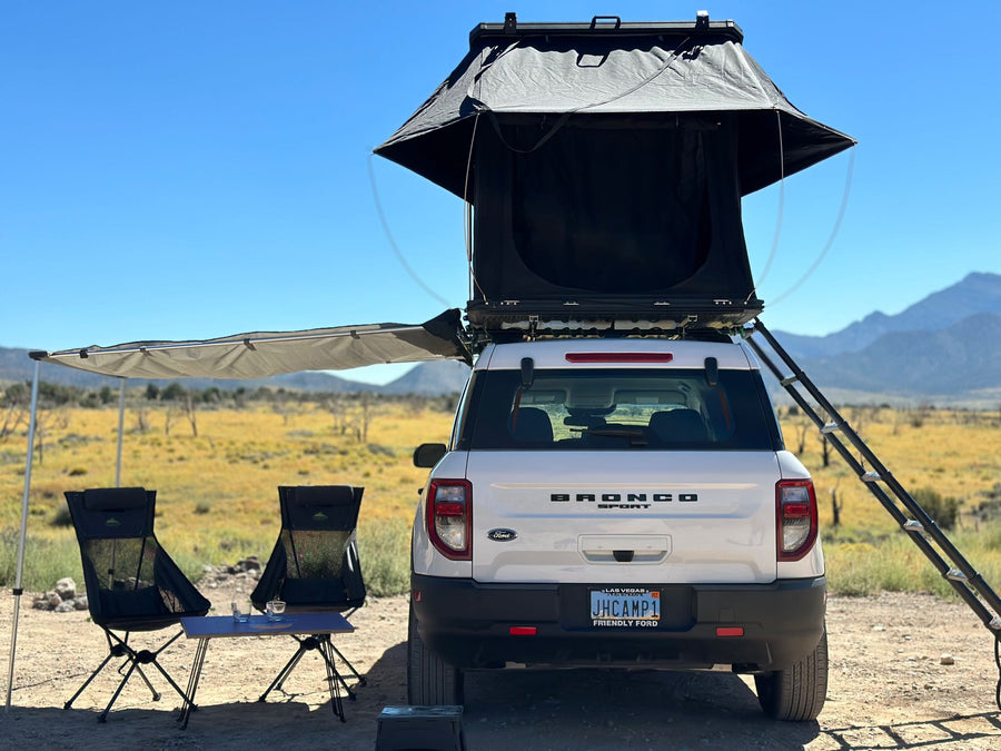 in a desert campsite at twilight. Consider this RV rental.|Scenic rv rental adventure: White Ford Bronco Sport with a NaturNest rooftop tent on a mountain trail.|White Ford Bronco Sport with rooftop tent & awning set up for camping. An RV rental alternative for desert overlanding.|A white Ford Bronco Sport with a rooftop tent at a desert campsite