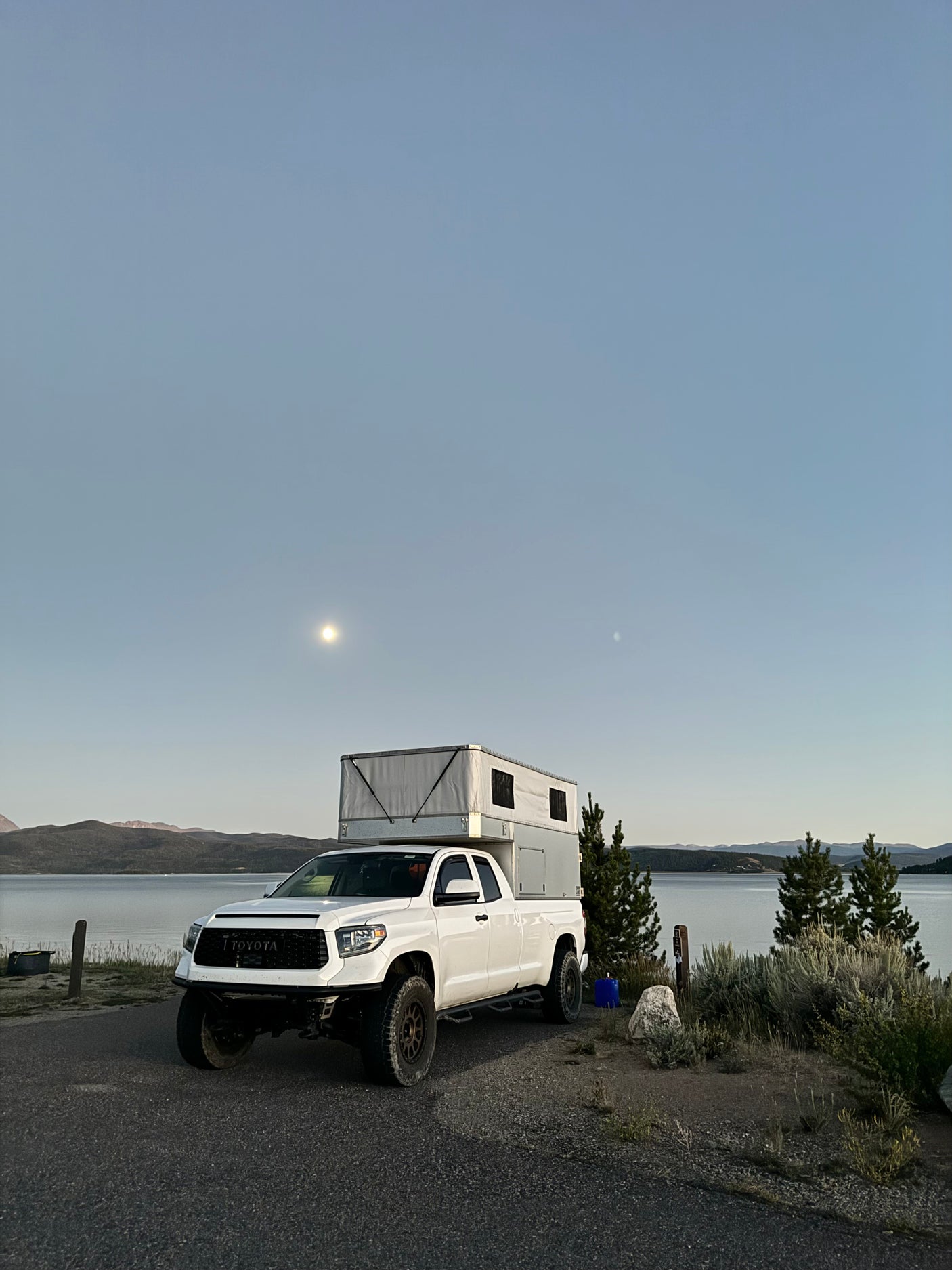 White Toyota Tundra with RV truck camper parked by a serene lake under a moonlit sky. Ideal for an rv rental adventure!