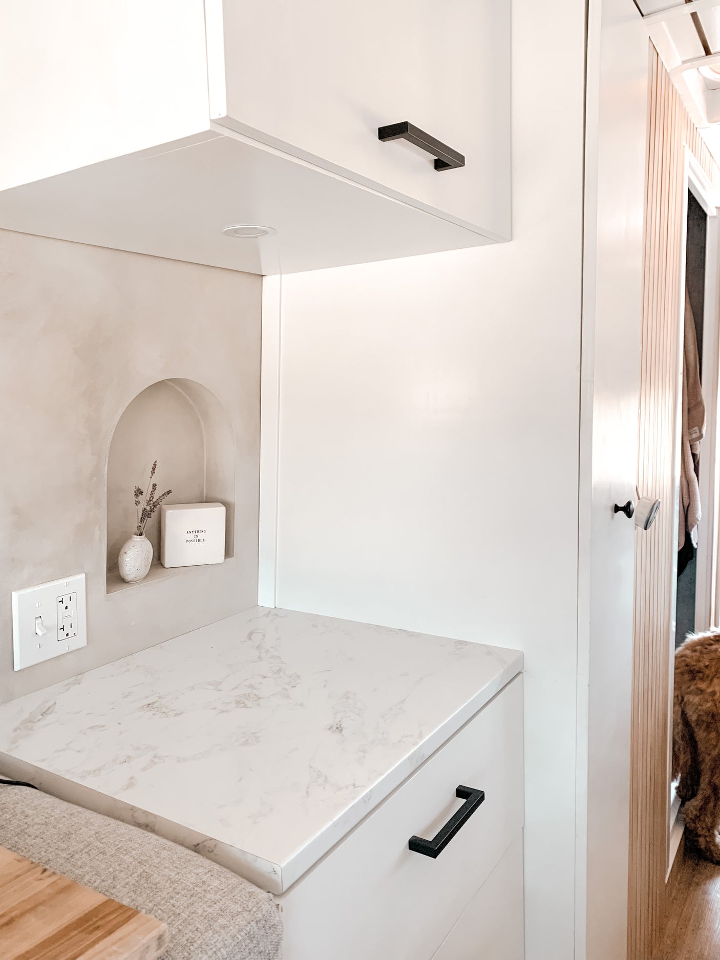 Modern RV rental kitchen with white cabinets, sleek black handles, marble-look counter, and a decorative wall niche.