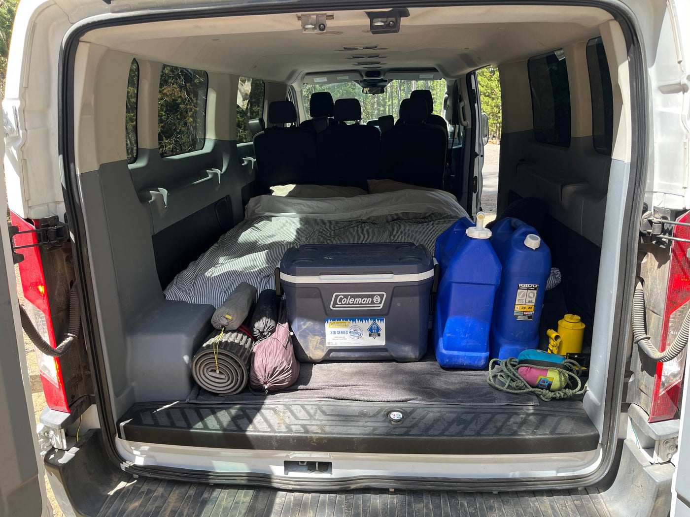 RV rental van's back packed with a bed, Coleman cooler, water jugs, and camping gear for an outdoor adventure. — photo 8